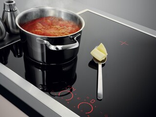 Noix de beurre reposant intacte sur la plaque froide à côté d’une casserole de sauce tomate en ébullition