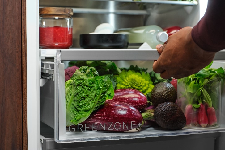 Homme tirant le tiroir GreenZone rempli de légumes à l'intérieur d'un réfrigérateur
