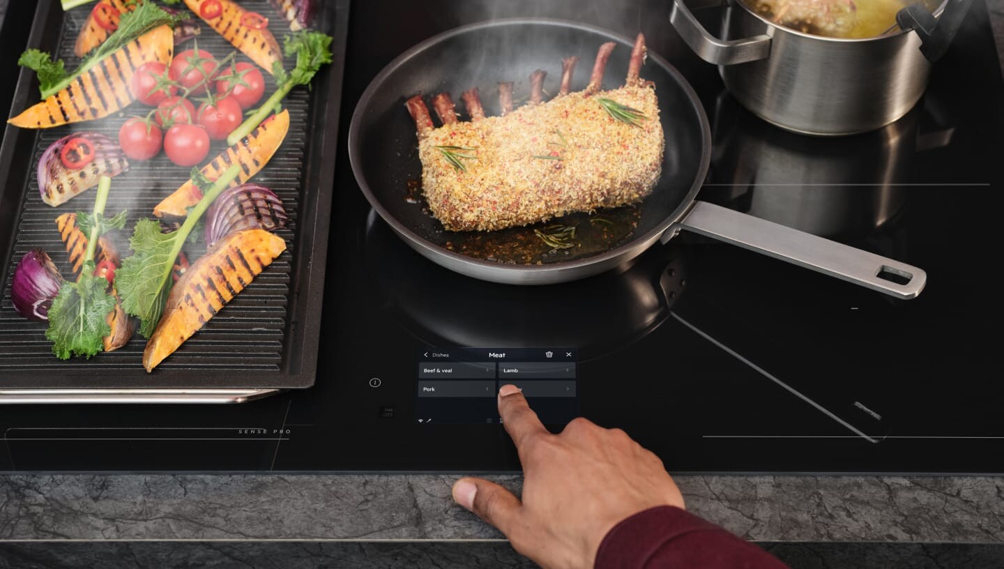 Un doigt touche le panneau de commande de la taque de cuisson à induction.