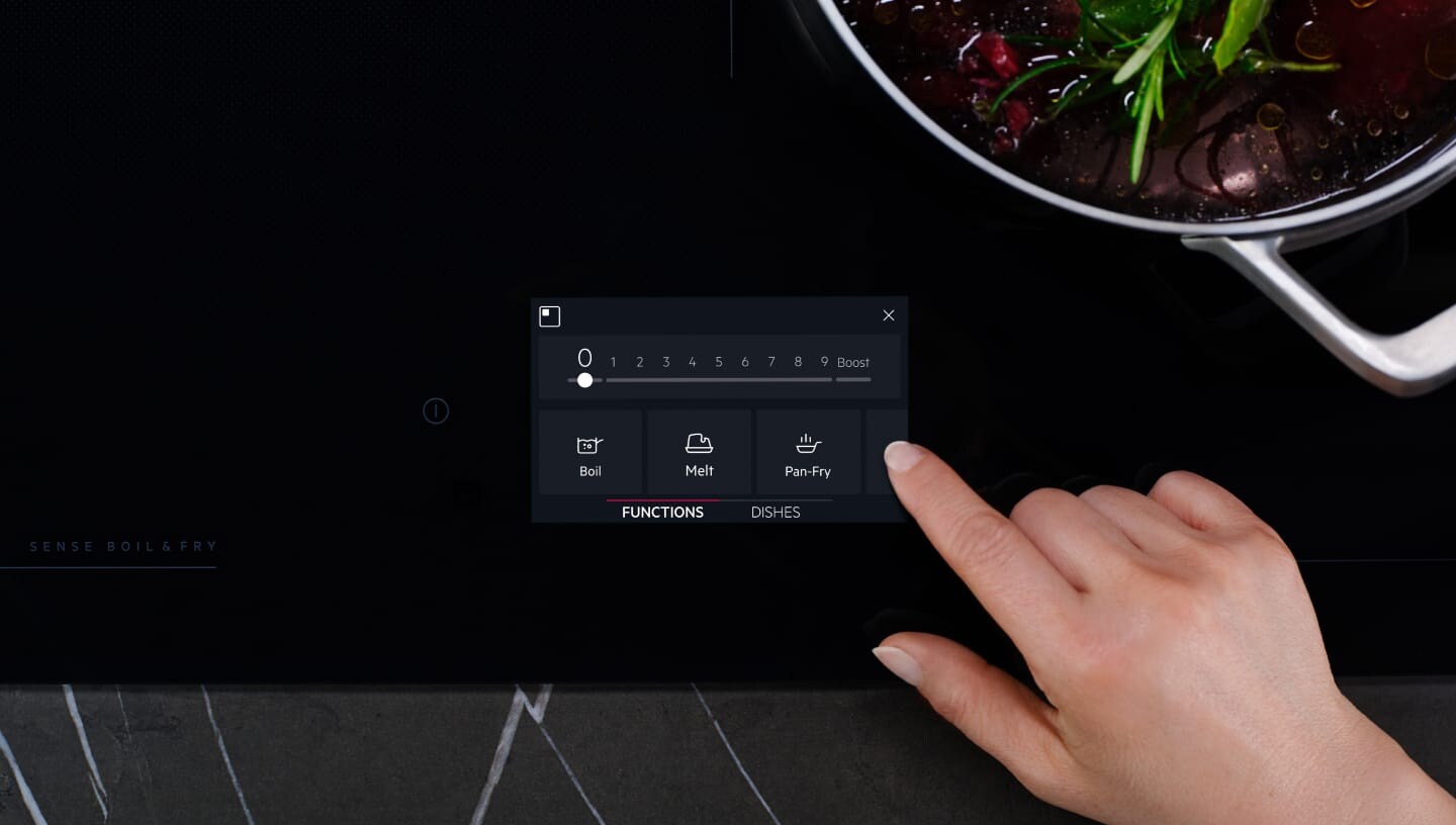 Un doigt touche le panneau de commande de la taque de cuisson à induction.