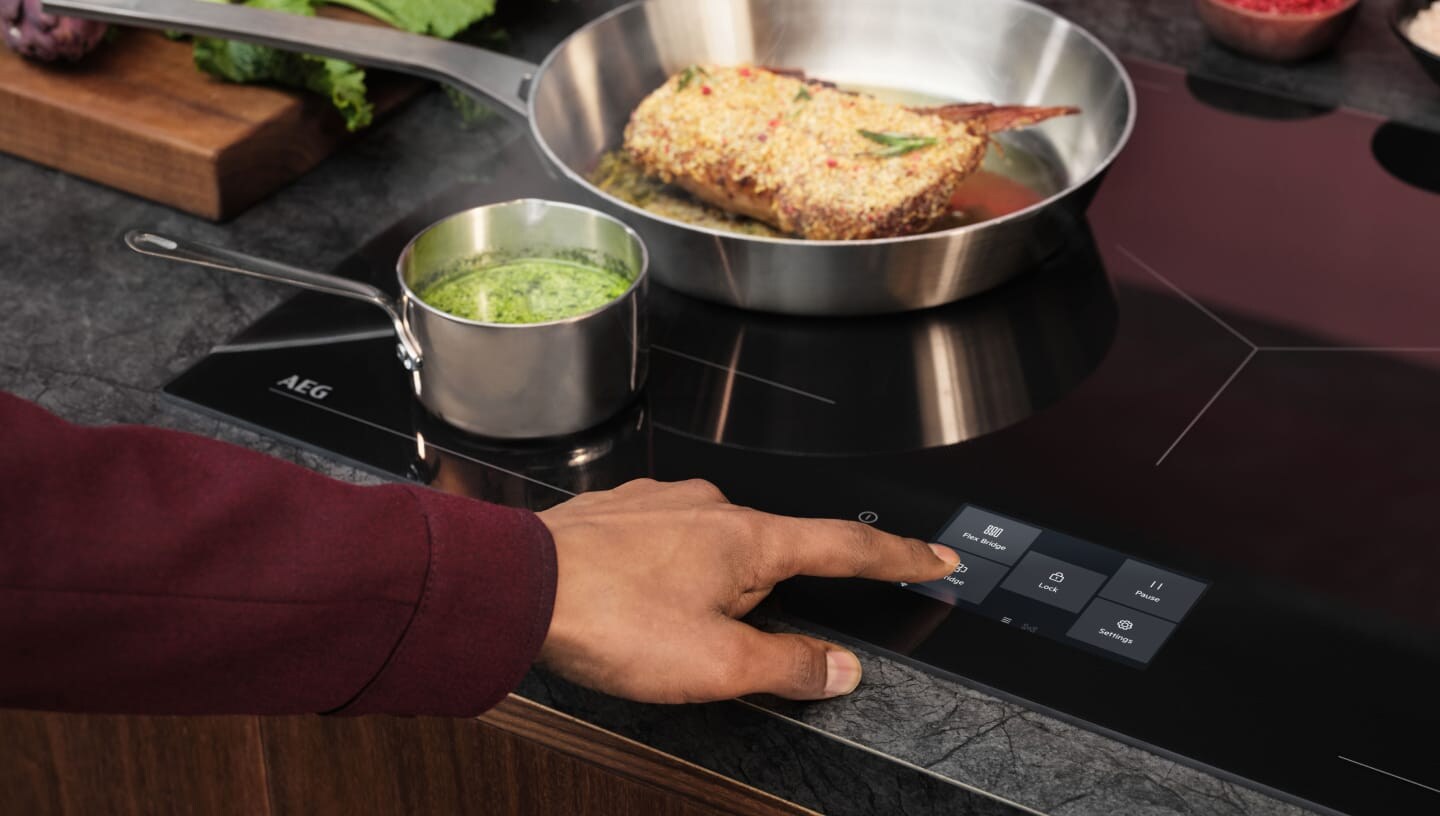 Un doigt touche le panneau de commande de la taque de cuisson à induction.