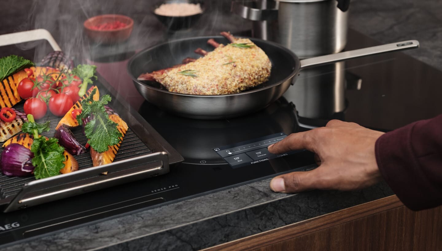 Un doigt touche le panneau de commande de la taque de cuisson à induction.