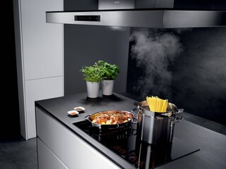 Nourriture en pleine cuisson sur une table à induction AEG pendant qu’une hotte aspirante extrait les excès de vapeur
