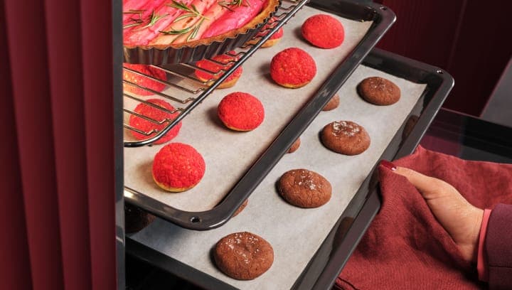 Une personne sort du four une plaque contenant des pâtisseries.