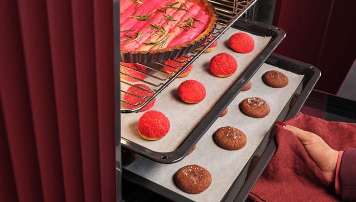 Une personne sort du four une plaque contenant des pâtisseries.