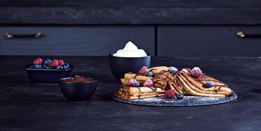 Piles de crêpes pliées nappées de sauce chocolat et recouvertes de fruits rouges