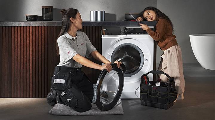 Repair woman replacing door for washing machine while young girl watches