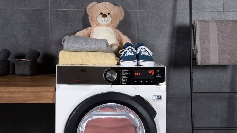 Ours en peluche placé avec des vêtements et des chaussures au-dessus d’une machine à laver AEG.