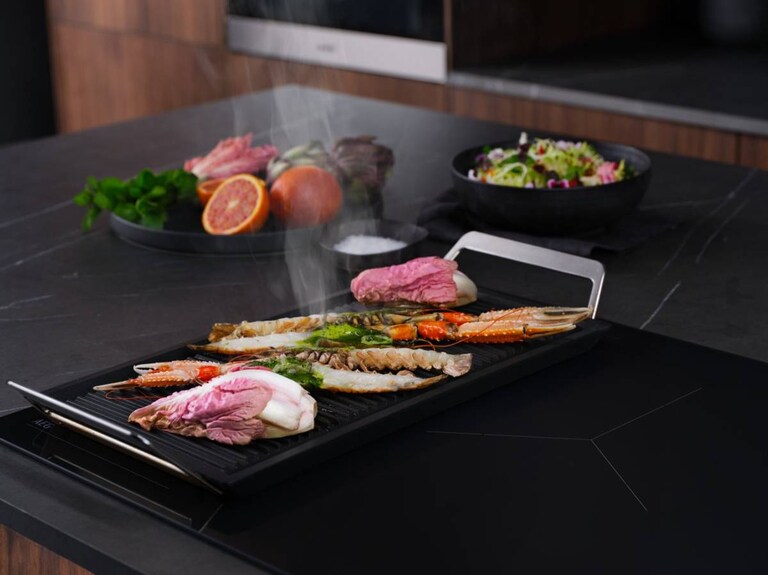 Une plaque de cuisson à induction AEG dotée d'une plaque de gril placha pour griller les aliments.